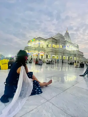 Pilgrim sitting in front of illuminated Prem Mandir Vrindavan at evening